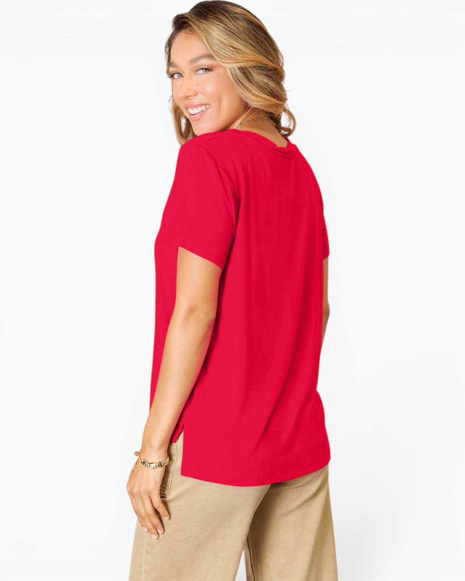 A woman wearing a bright red short-sleeve t-shirt and beige pants, shown from a side-back angle against a plain white studio background.