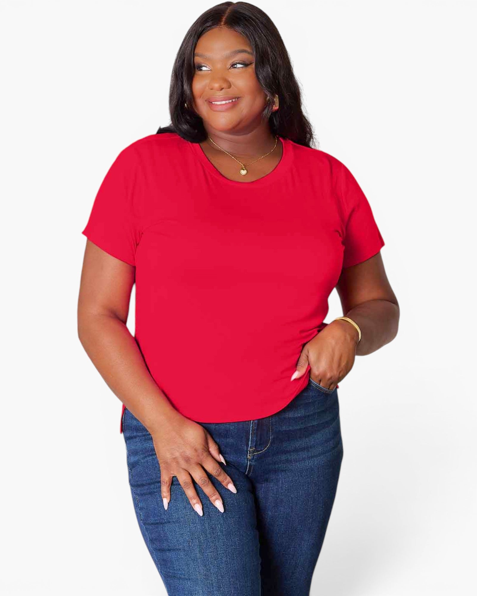 A woman modeling a bright red short-sleeve crewneck t-shirt paired with blue jeans, standing against a light gray studio background.