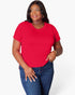 A woman modeling a bright red short-sleeve crewneck t-shirt paired with blue jeans, standing against a light gray studio background.