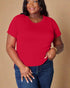 Woman wearing a red t-shirt and blue jeans against a beige background