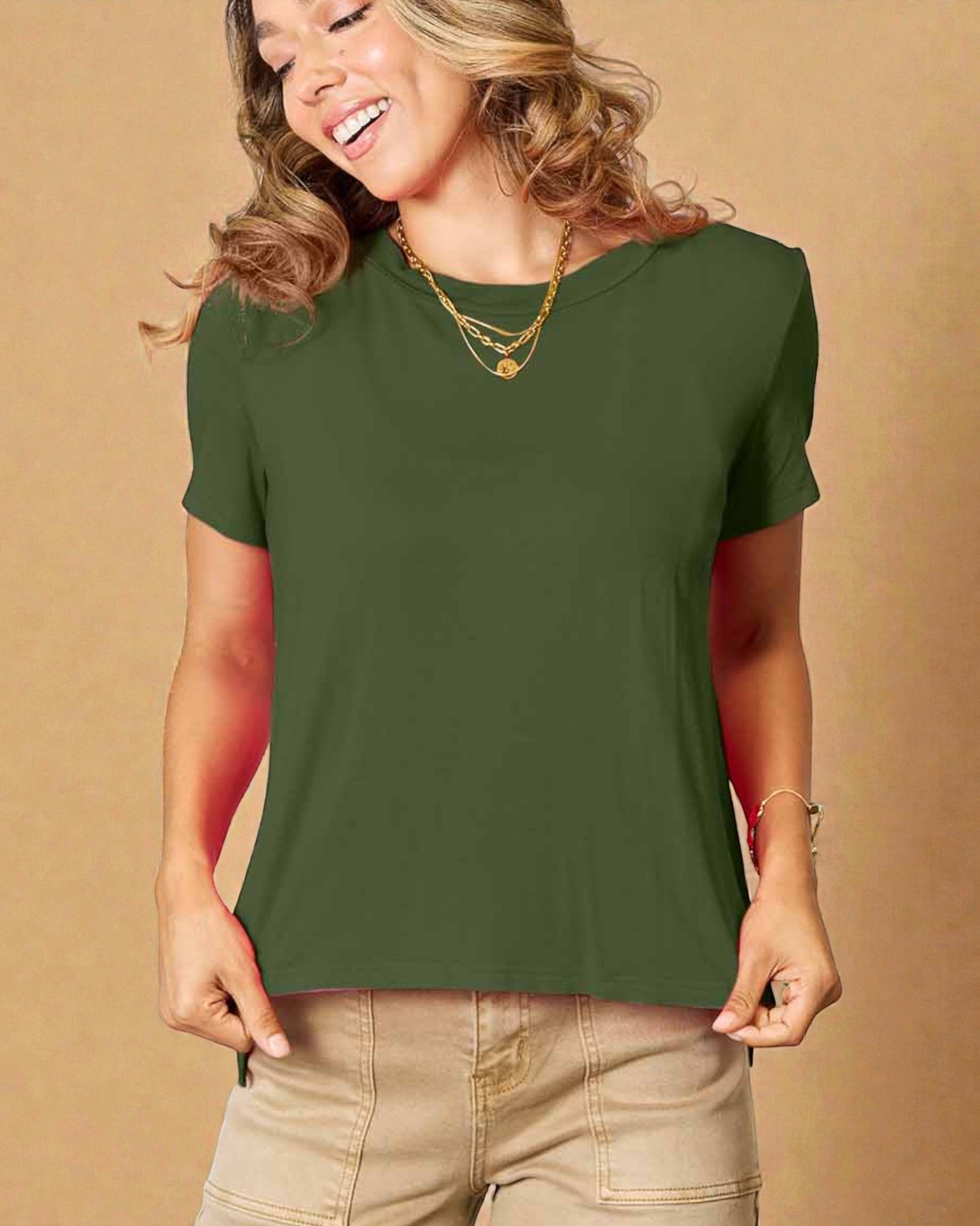 Woman wearing a green t-shirt and beige pants against a beige background
