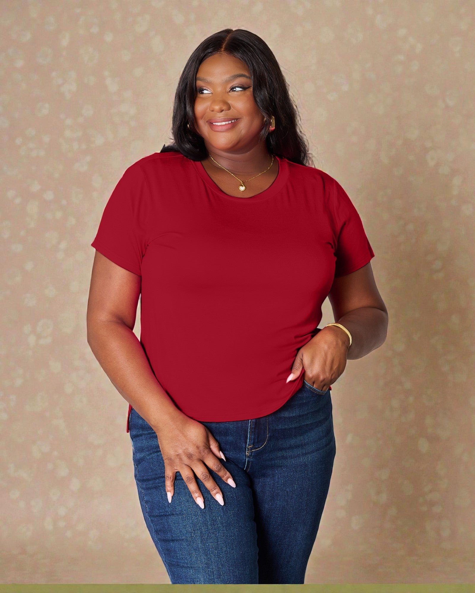 Woman wearing a red shirt and blue jeans against a beige background