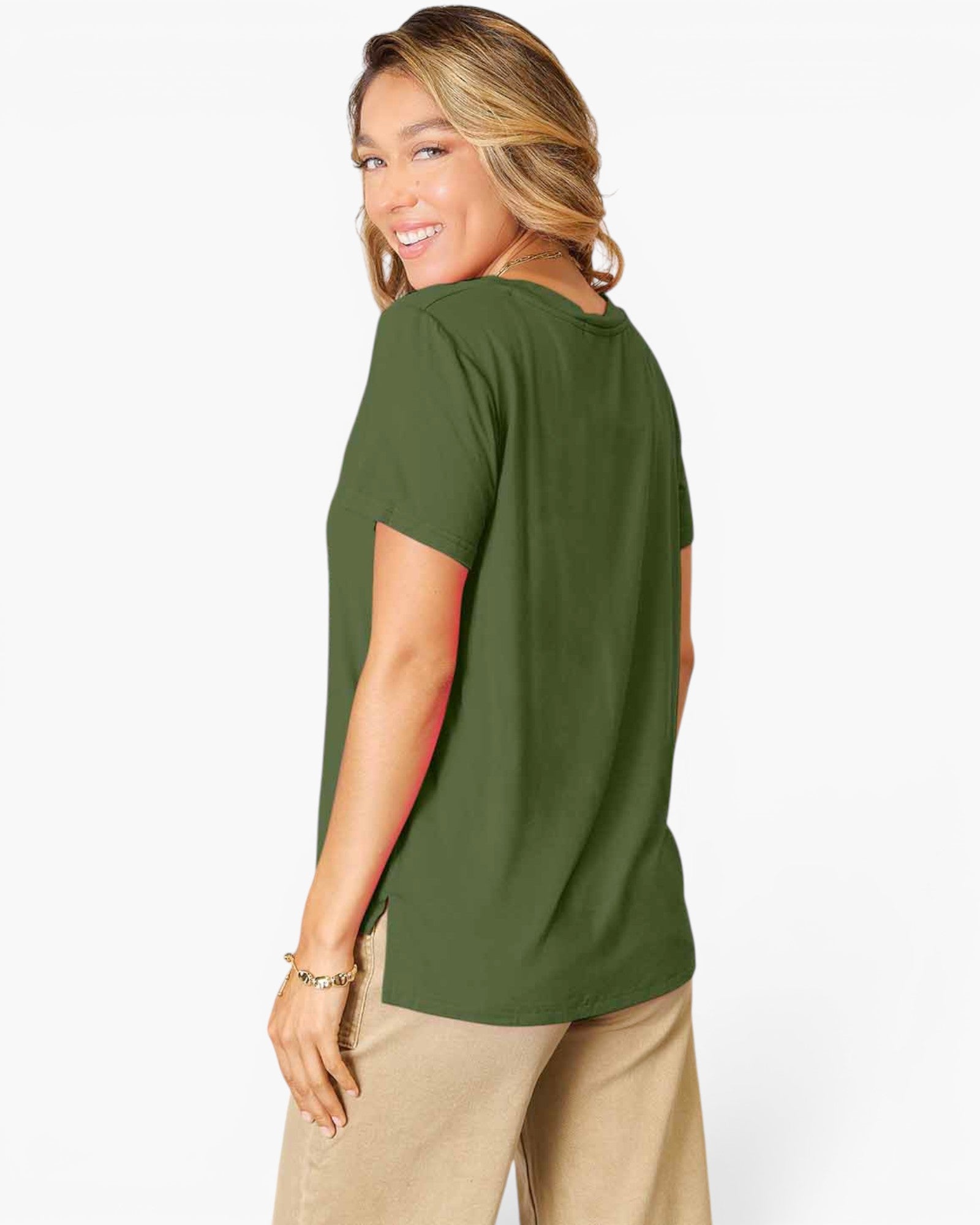 A woman wearing an olive green short-sleeve t-shirt and beige pants, shown from a side-back angle against a plain white studio background.