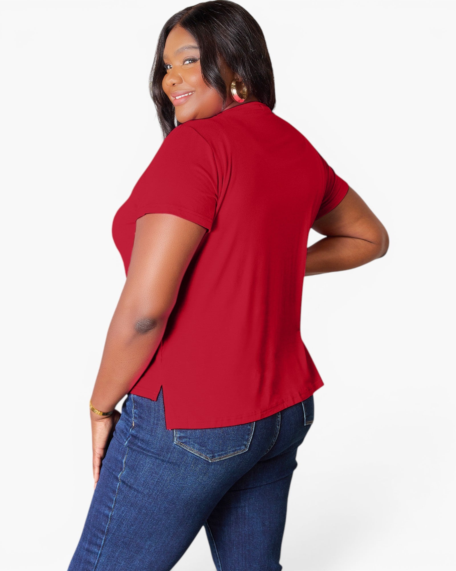 A woman wearing a red short-sleeve top and blue jeans, photographed from the back against a light gray studio background.