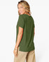 A woman wearing an olive green short-sleeve t-shirt and beige pants, shown from a side-back angle against a plain white studio background.