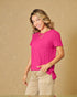 Woman wearing a bright pink shirt and beige pants against a beige background