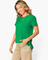 A woman wearing a bright green short-sleeve top and beige pants, posing against a light gray studio background.