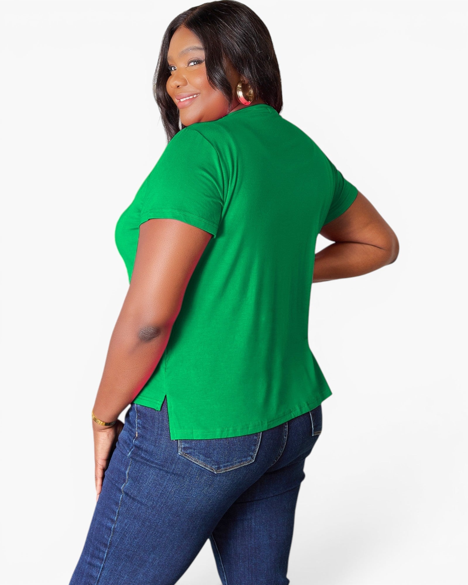 A woman wearing a bright green short-sleeve t-shirt and blue jeans, shown from a three-quarters back view against a light gray studio background.