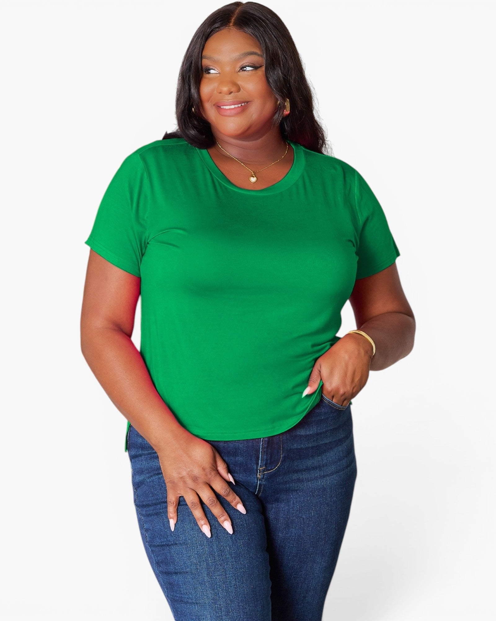 A woman modeling a bright green short-sleeve crewneck t-shirt paired with dark blue jeans, standing against a light gray studio background.