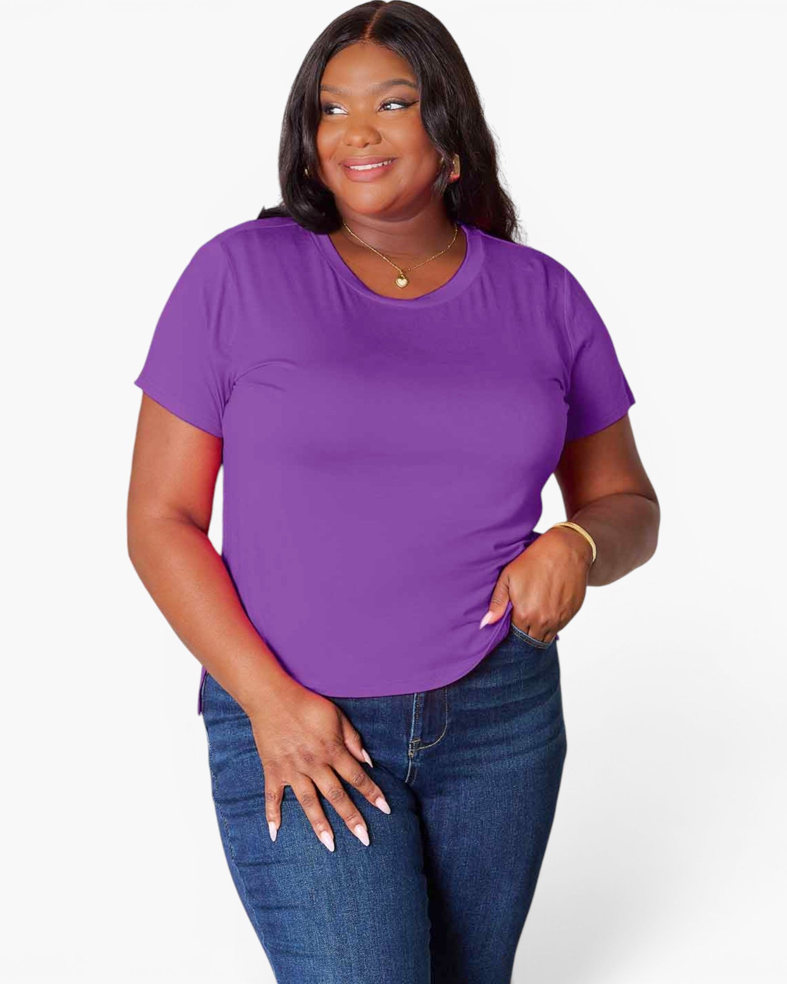 A woman modeling a short-sleeve crewneck t-shirt in solid purple, paired with dark blue jeans, against a light gray studio background.
