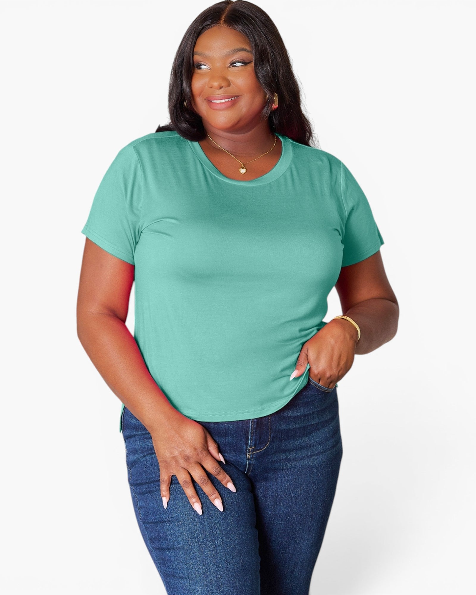 A woman modeling a short-sleeve crewneck t-shirt in a mint green color, paired with dark blue jeans, against a plain light gray background.