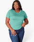 A woman modeling a short-sleeve crewneck t-shirt in a mint green color, paired with dark blue jeans, against a plain light gray background.