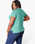 A woman wearing a mint green short-sleeve t-shirt and blue jeans, photographed from the back against a light gray studio background.