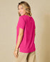Woman wearing a bright pink t-shirt and beige pants against a beige background