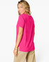 A woman wearing a bright pink short-sleeve t-shirt and beige pants, shown from a side-back angle against a clean white studio background.