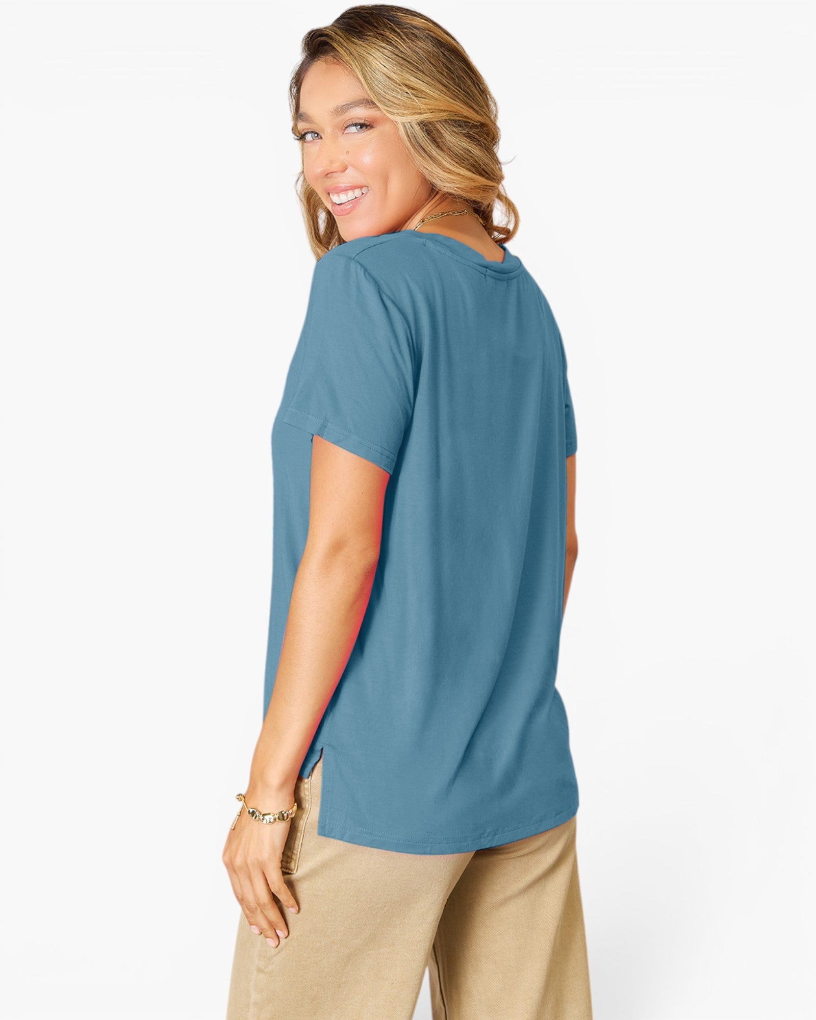A woman wearing a short-sleeve blue t-shirt and beige pants, shown from a side-back angle against a plain white studio background.