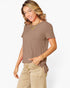 A woman wearing a taupe brown short-sleeve t-shirt and beige pants, posing against a light gray background.