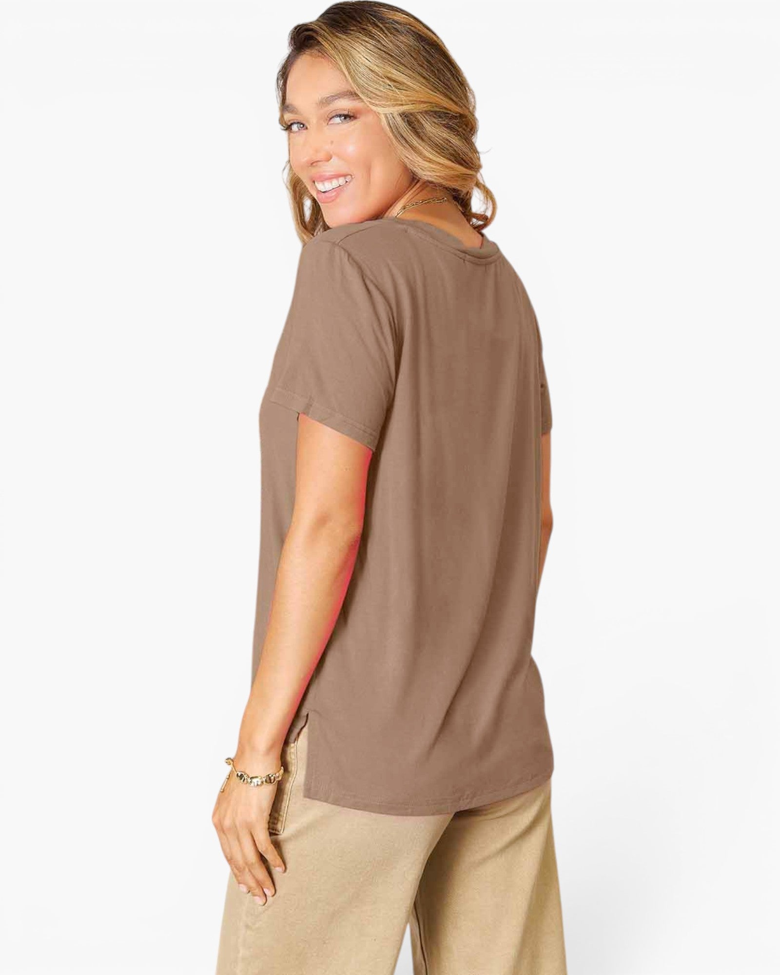 A woman wearing a brown short-sleeve t-shirt and beige pants, shown from a side-back angle against a plain white studio background.