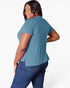 A woman modeling a short-sleeve teal blue top from the back, paired with dark blue jeans, against a plain white studio background.