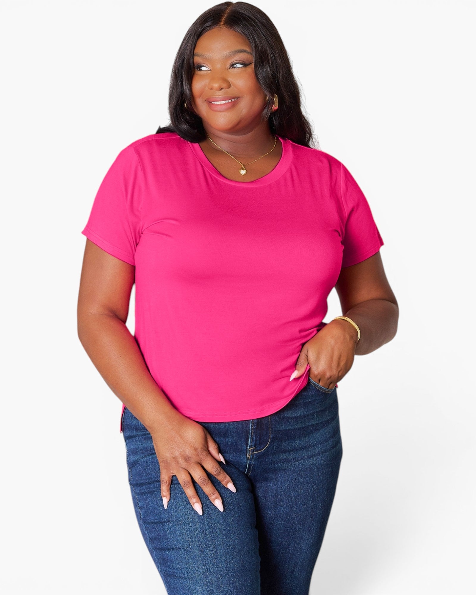 A woman modeling a bright pink short-sleeve crewneck t-shirt paired with dark blue jeans, photographed against a clean white studio background.