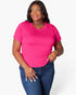A woman modeling a bright pink short-sleeve crewneck t-shirt paired with dark blue jeans, photographed against a clean white studio background.