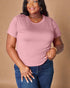 Woman wearing a pink t-shirt and blue jeans against a beige background