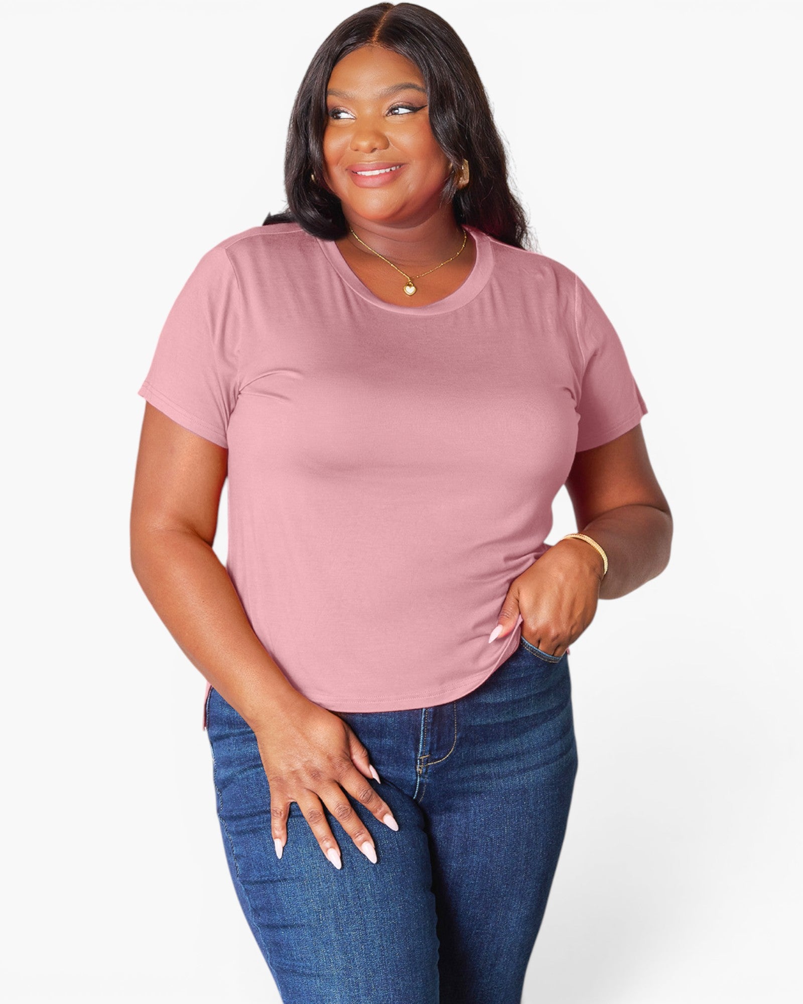 A woman modeling a short-sleeve crewneck t-shirt in dusty pink, paired with dark blue jeans, against a plain white studio background.