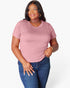 A woman modeling a short-sleeve crewneck t-shirt in dusty pink, paired with dark blue jeans, against a plain white studio background.