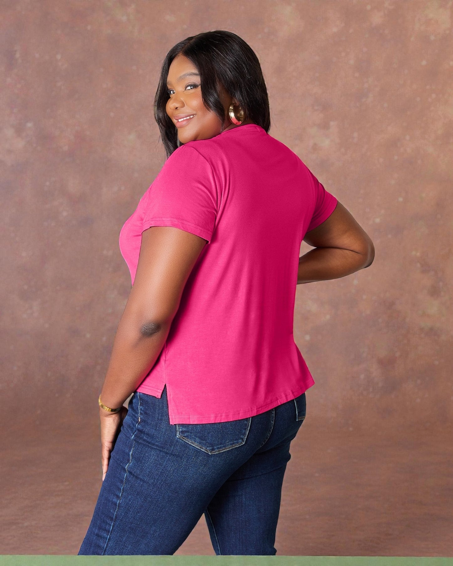 Woman wearing a pink shirt and blue jeans against a brown background