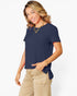 A woman modeling a navy blue short-sleeve top with a side tie detail, paired with beige pants, against a plain white background.