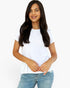 A woman with long dark hair wearing a white short-sleeve crewneck t-shirt and light blue jeans, standing against a plain white background.