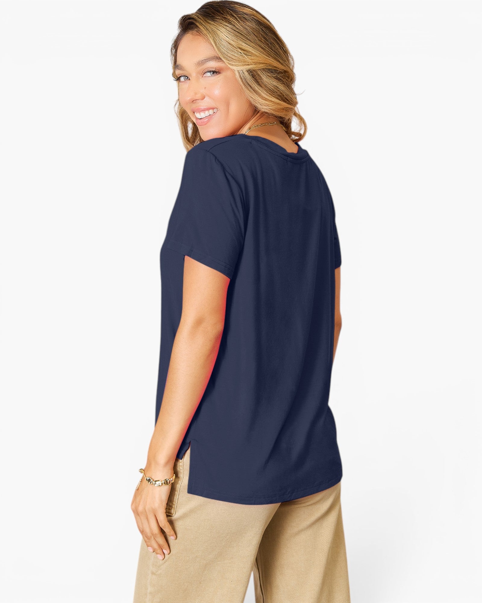 A woman wearing a navy blue short-sleeve t-shirt and beige pants, shown from a three-quarters back view against a plain white studio background.