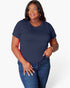 A woman modeling a navy blue short-sleeve crewneck t-shirt with dark blue jeans, standing against a light gray studio background.