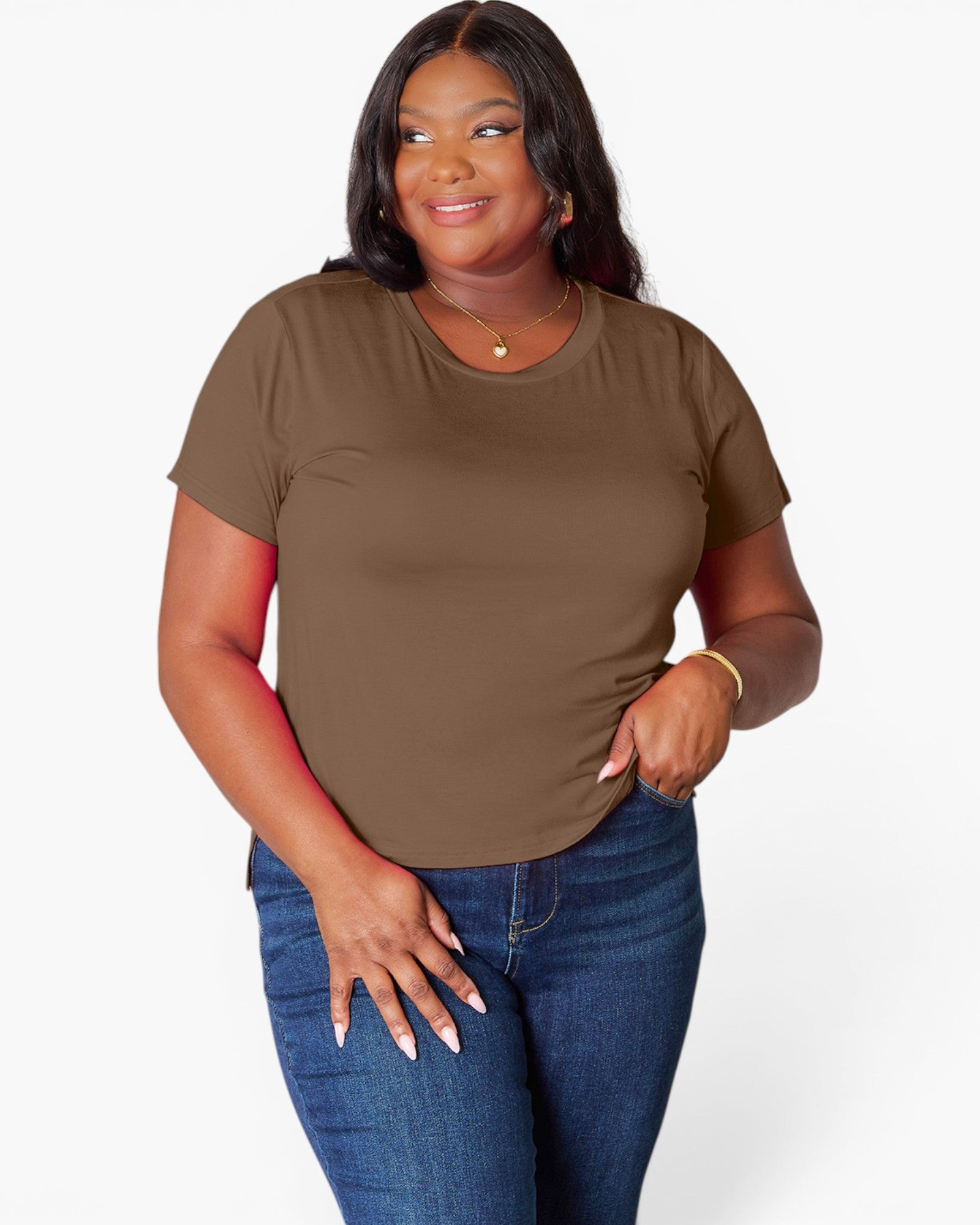 A woman modeling a short-sleeve crewneck t-shirt in solid brown, paired with blue jeans, against a light gray studio background.