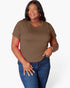A woman modeling a short-sleeve crewneck t-shirt in solid brown, paired with blue jeans, against a light gray studio background.