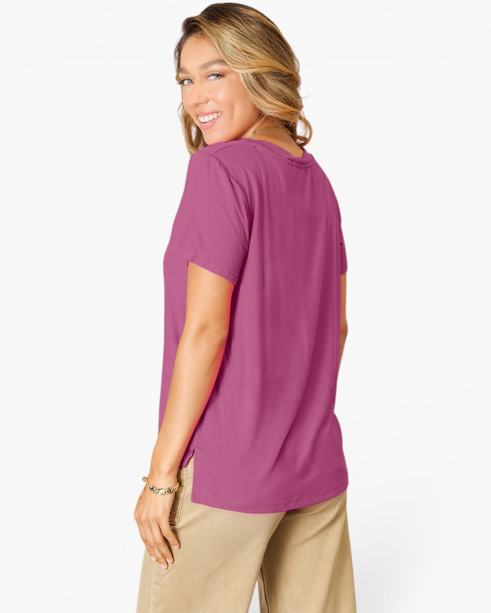 A woman wearing a short-sleeve crewneck t-shirt in a dusty magenta-purple color, paired with beige pants, photographed from a side-back angle against a clean white background.