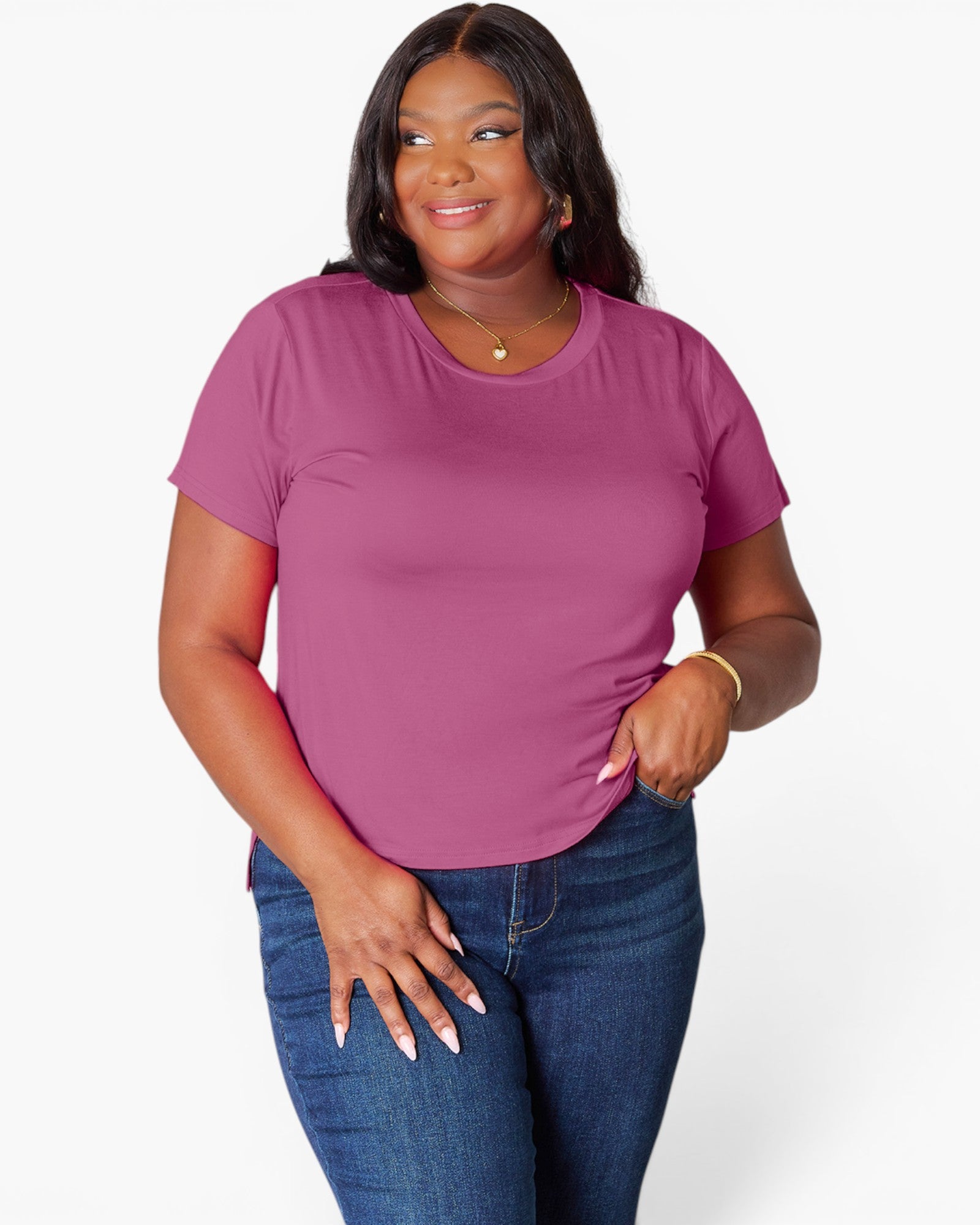 A woman modeling a short-sleeve crewneck t-shirt in a dusty magenta pink color, paired with blue jeans, against a clean white studio background.