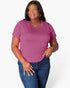 A woman modeling a short-sleeve crewneck t-shirt in a dusty magenta pink color, paired with blue jeans, against a clean white studio background.
