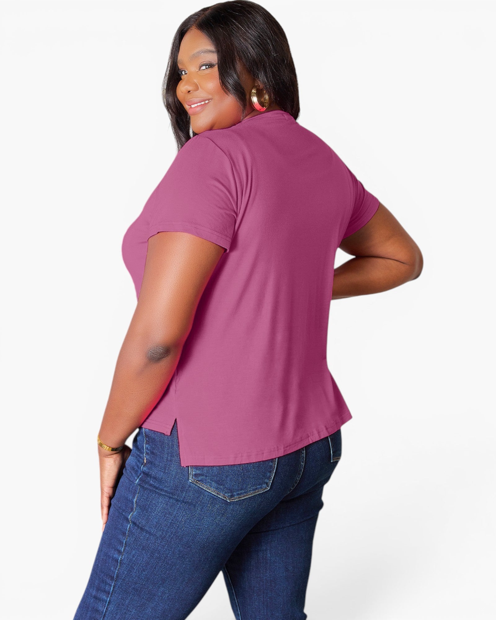 A woman modeling a short-sleeve magenta pink top from the back, paired with blue jeans, against a plain white studio background.