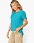 A woman wearing a bright turquoise short-sleeve top and beige pants, posing against a clean white background.