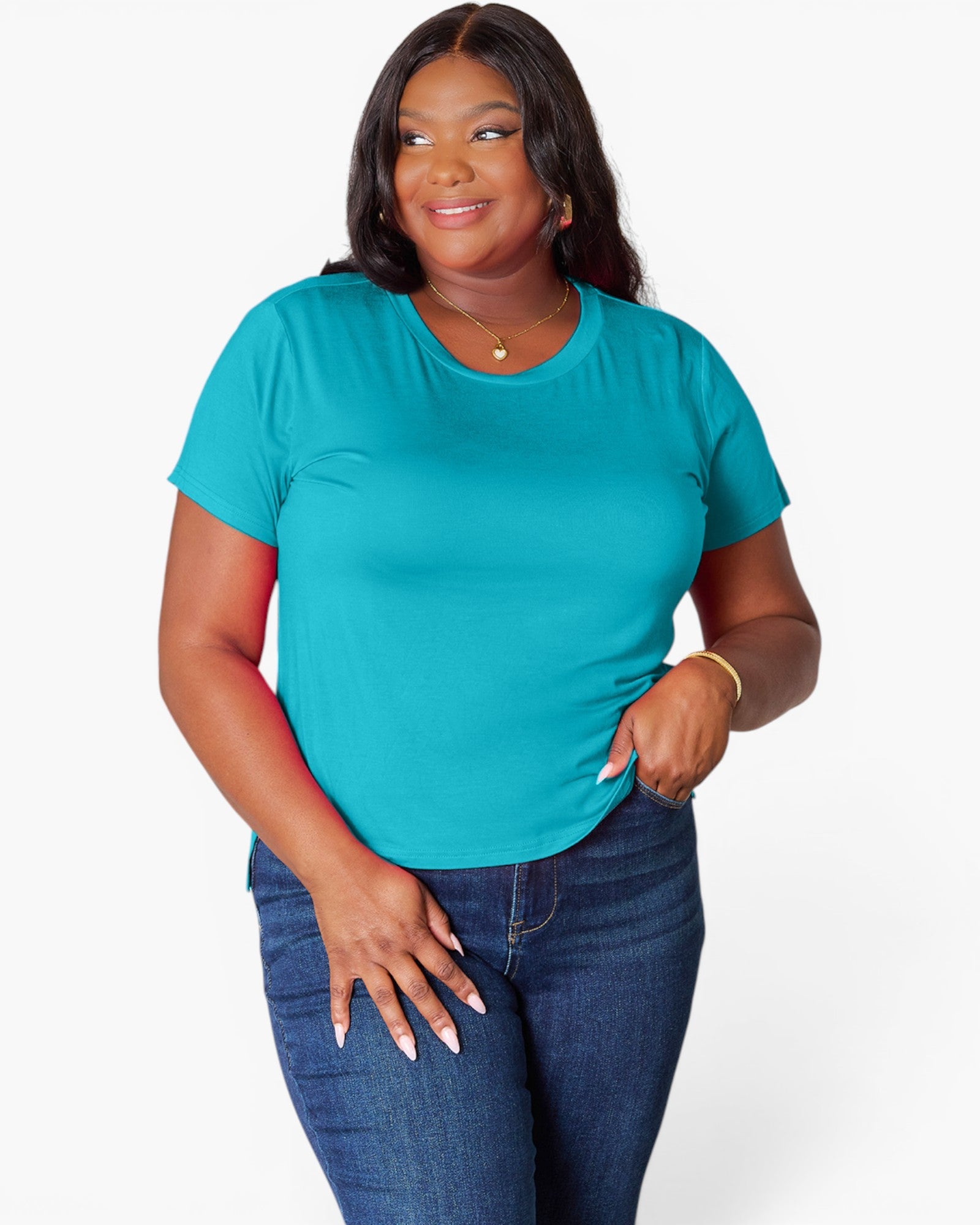 A woman modeling a bright teal short-sleeve crewneck t-shirt paired with dark blue jeans, standing against a light gray studio background.