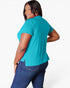 A woman wearing a bright turquoise short-sleeve top and dark blue jeans, photographed from the back against a clean white studio background.