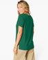 A woman wearing a dark green short-sleeve t-shirt and beige pants, shown from a side-back angle against a light gray studio background.