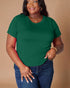 Woman wearing a green t-shirt and blue jeans against a beige background