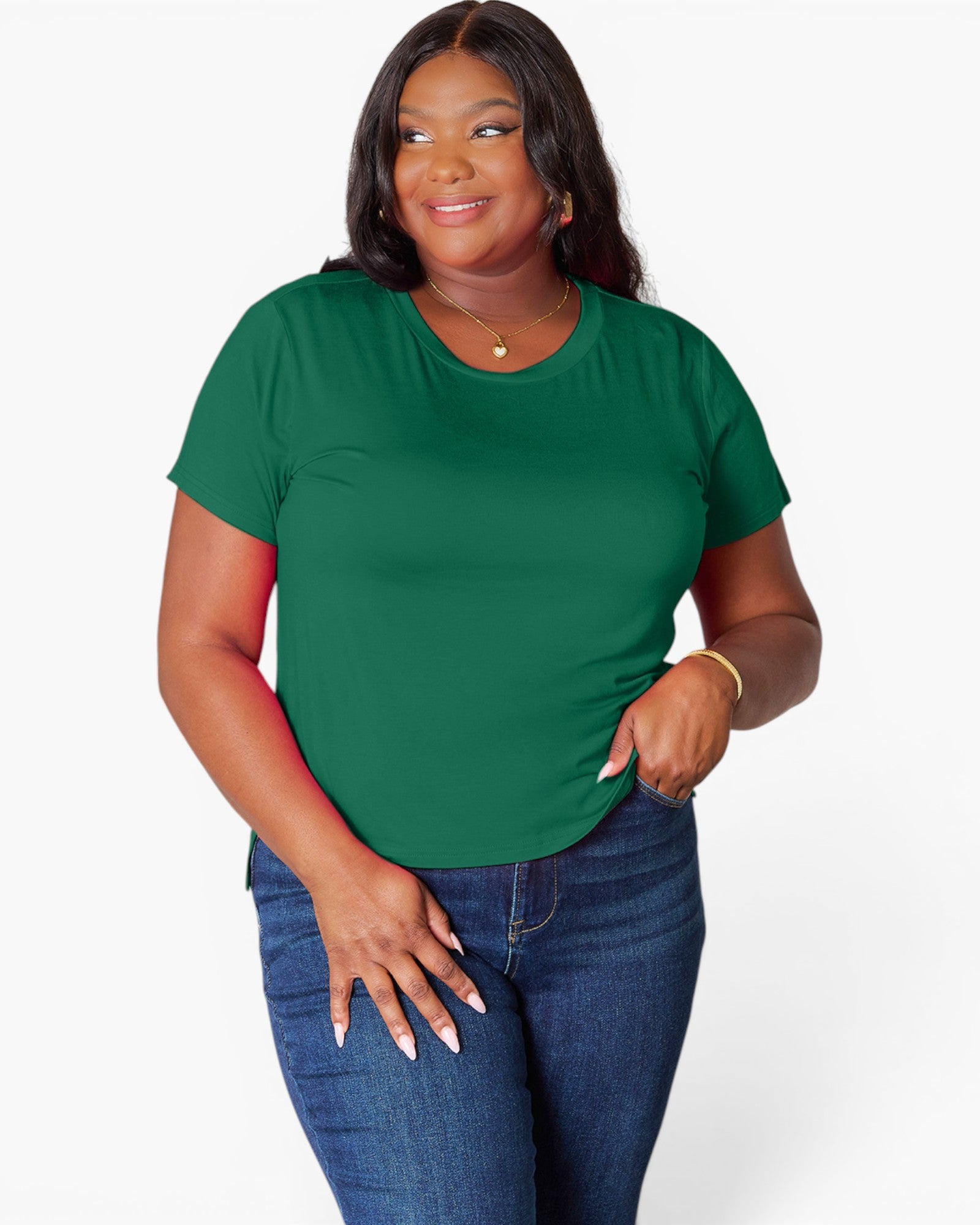 A woman modeling a short-sleeve crewneck t-shirt in forest green, paired with blue jeans, against a plain light gray background.