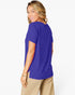 A woman wearing a short-sleeve royal blue top and beige pants, photographed from the back against a clean white studio background.