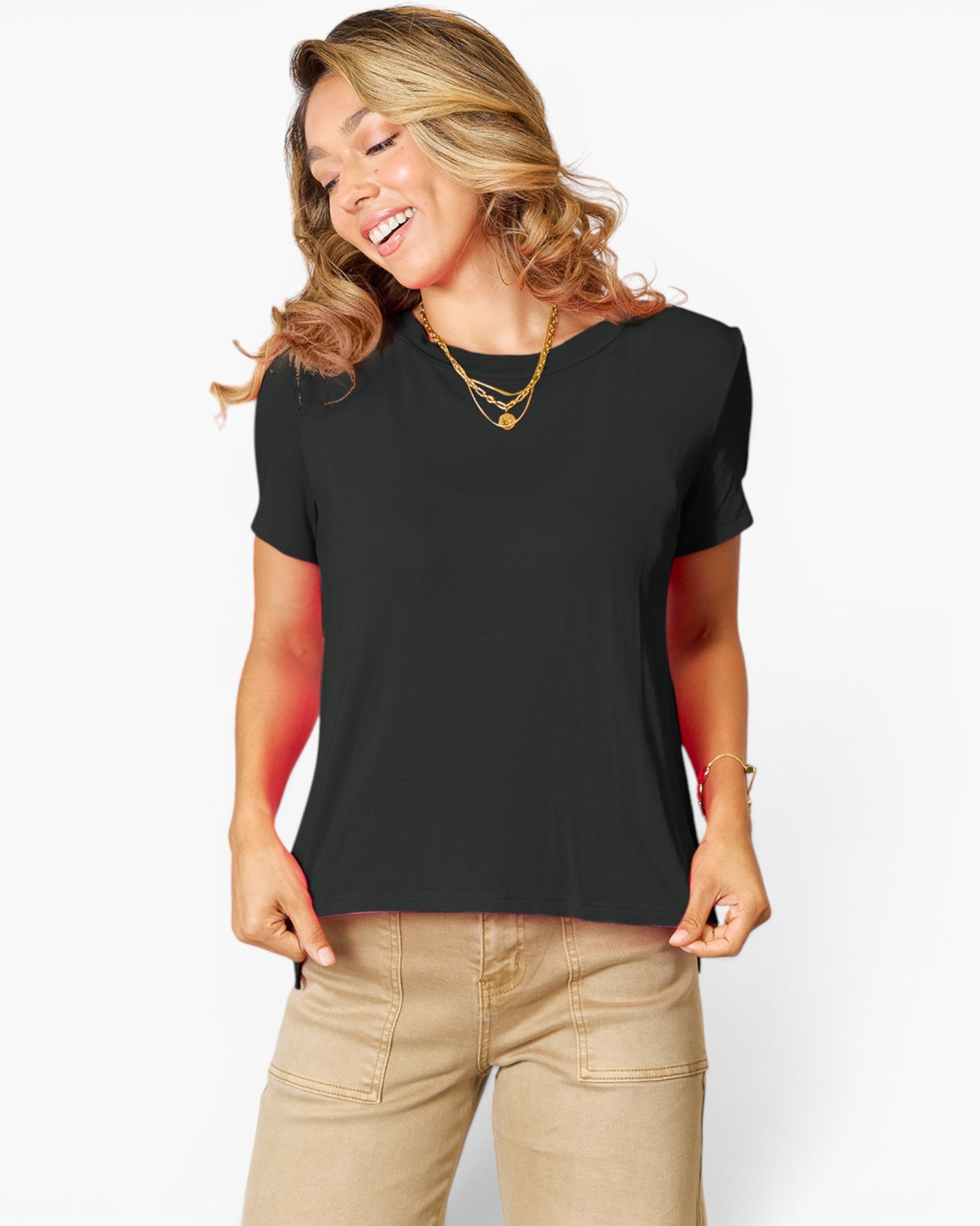 A woman wearing a black short-sleeve scoop-neck t-shirt and beige pants, posing against a light gray background.