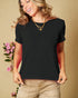 Woman wearing a black t-shirt and beige pants against a beige background with pink flowers.