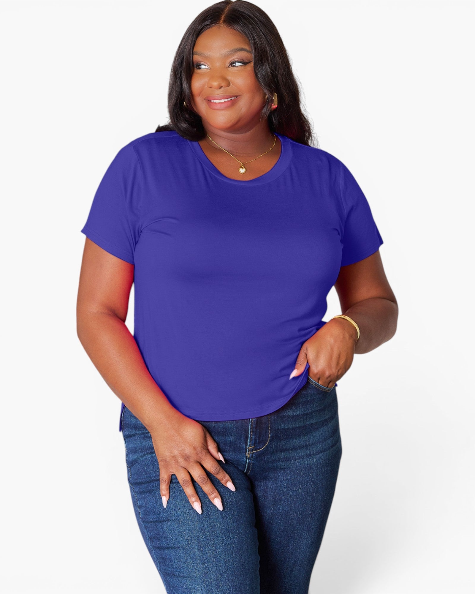 A woman modeling a short-sleeve crewneck t-shirt in a vibrant purple color, paired with dark blue jeans, against a plain light gray background.