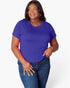 A woman modeling a short-sleeve crewneck t-shirt in a vibrant purple color, paired with dark blue jeans, against a plain light gray background.